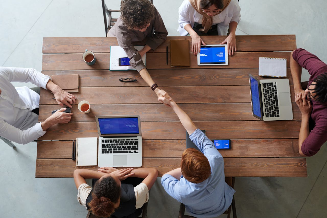 people at desk with laptop crossing over to shake hands